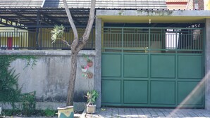 Een woonhuis met een groene garage, een boom ervoor en bloempotten aan de muur.