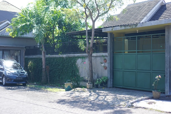 Zona residencial con un automóvil estacionado, un árbol y una puerta de garaje verde.