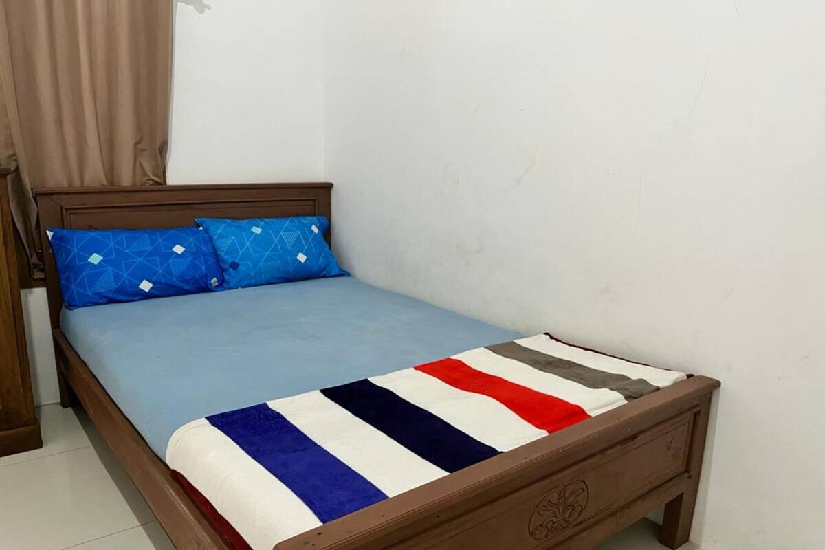 A single bed with a wooden frame, a blue mattress, and a striped blanket.
