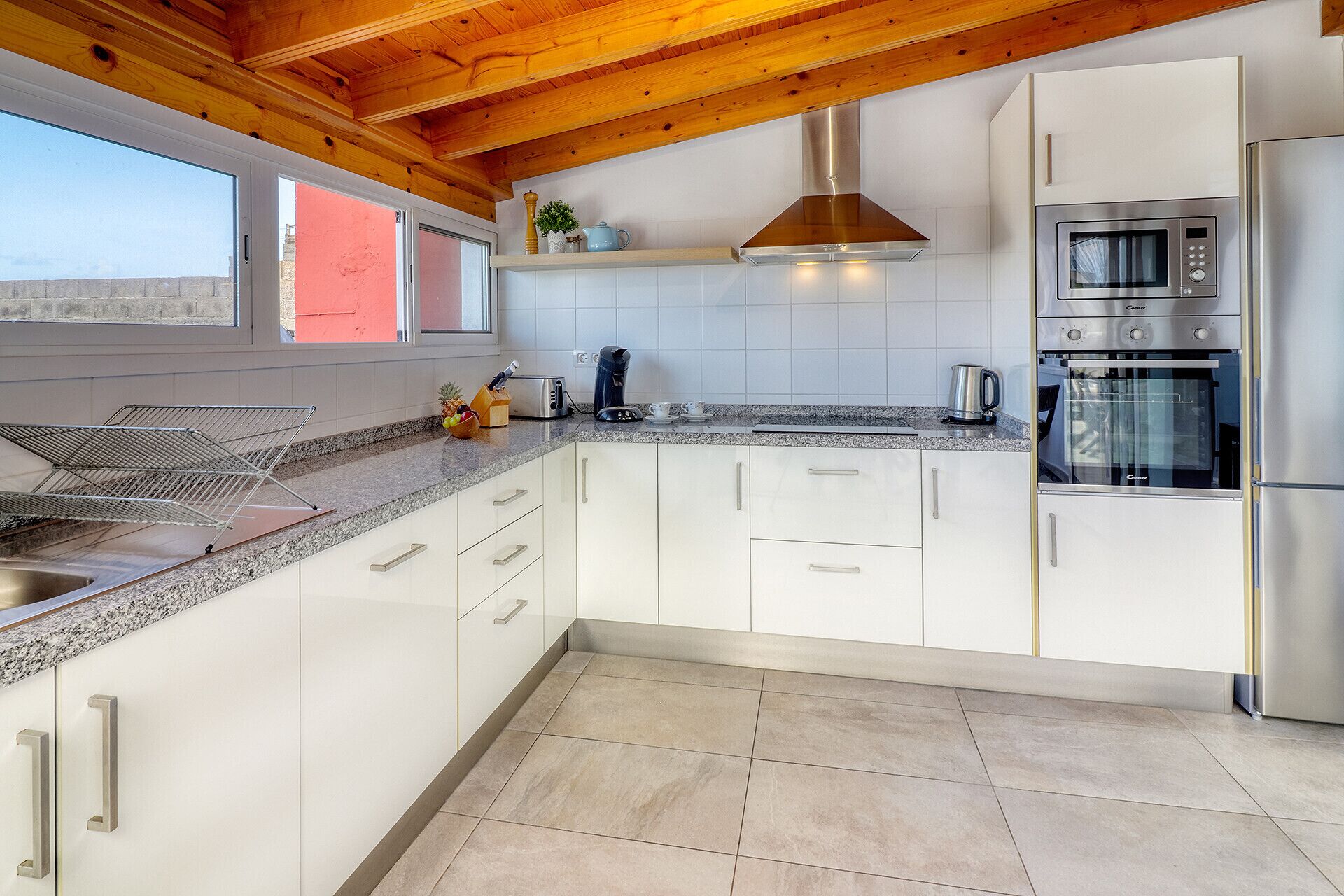Una cocina moderna con armarios blancos, electrodomésticos de acero inoxidable y techo de madera.