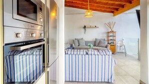 A modern kitchen with a built-in oven and microwave, a striped sofa set, a wooden ceiling, and a hanging light fixture.