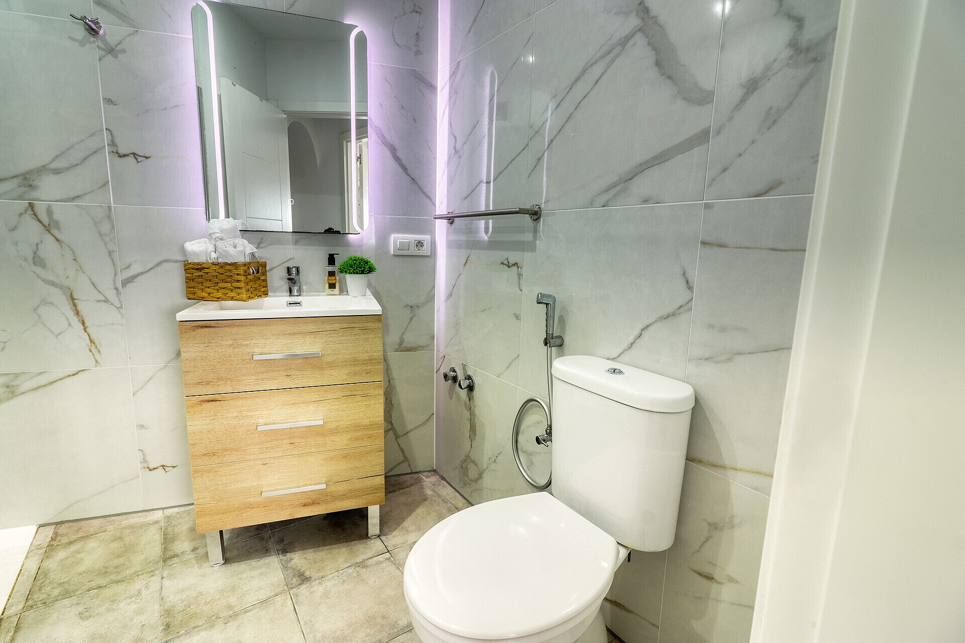Un baño moderno con pared de mármol, tocador de madera con cajones, inodoro blanco y cabina de ducha de vidrio.