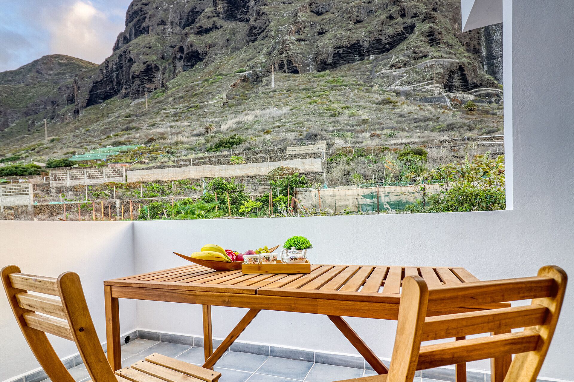 Mesa y sillas de madera en un balcón con vista a la montaña.