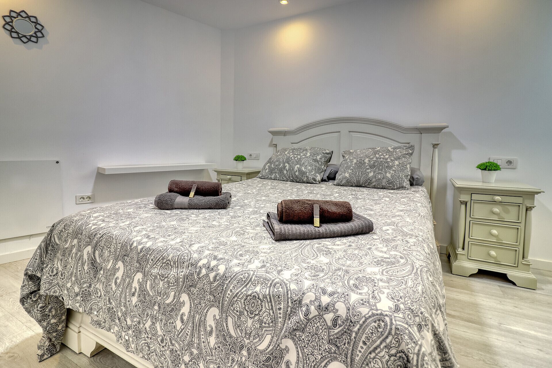 Una cama bien hecha con una colcha estampada, dos almohadas y dos toallas enrolladas sobre la cama.