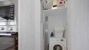 Uma área de lavanderia compacta com máquina de lavar, micro-ondas e um pequeno ferro de passar.