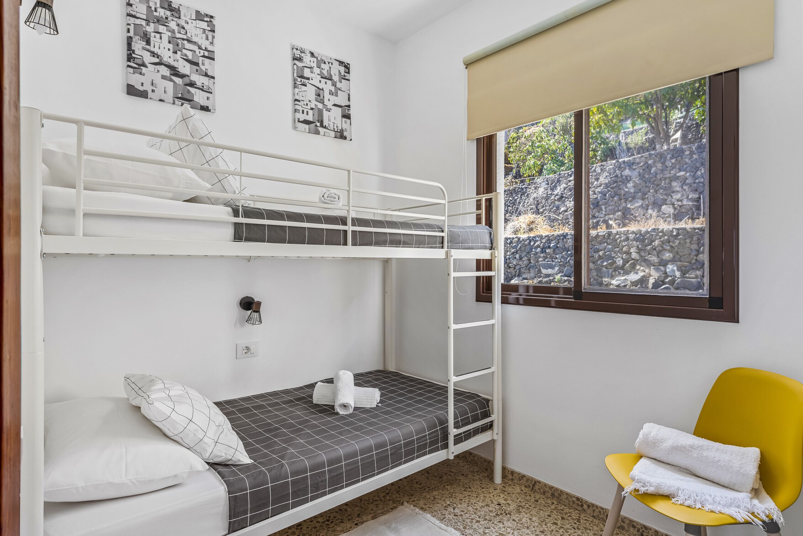 Une chambre avec un lit superposé, une fenêtre, une chaise jaune et deux œuvres d’art murales.