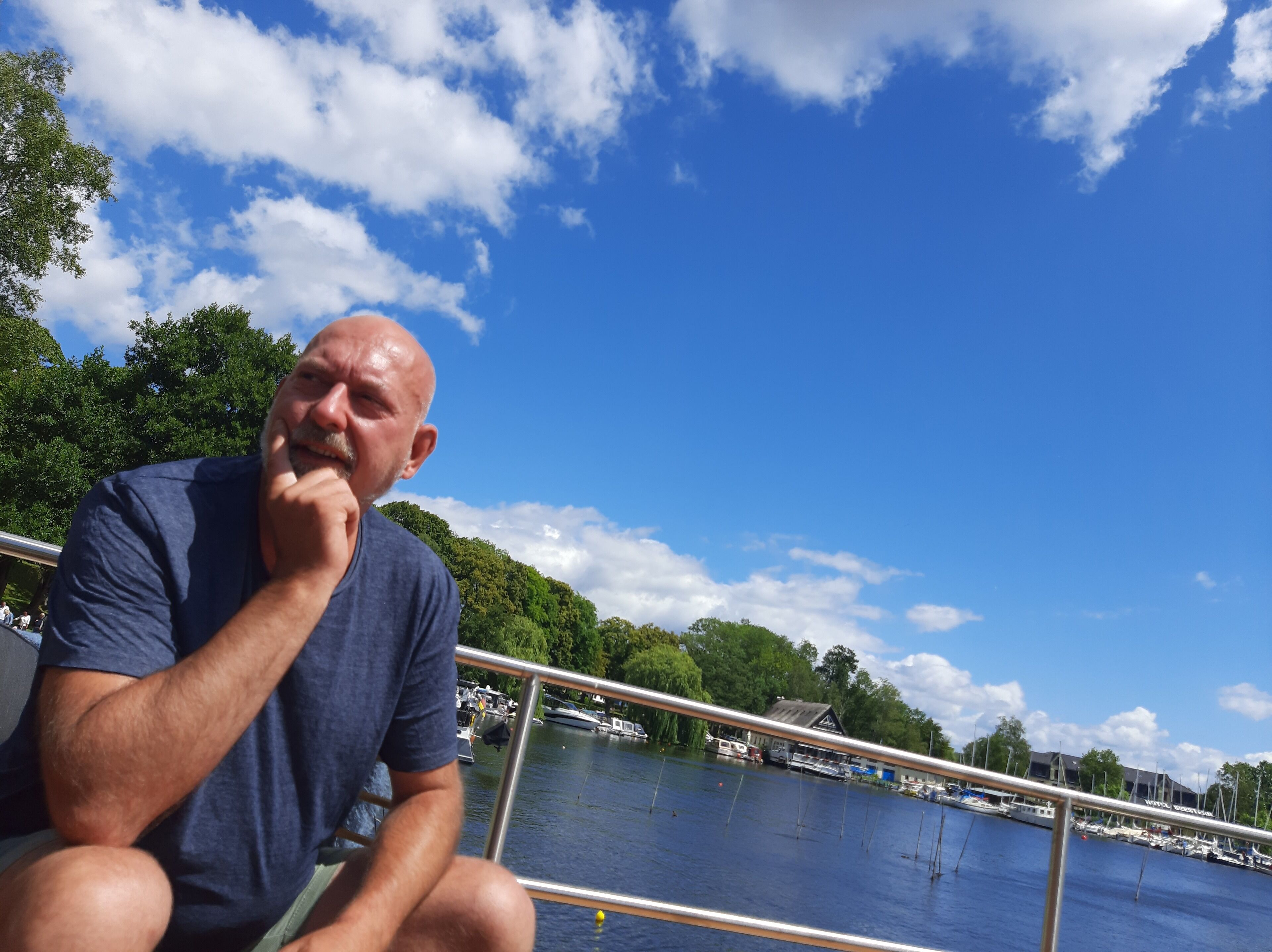 Un homme est assis sur un bateau, avec une vue sur une marina et sur d’autres bateaux amarrés au loin.