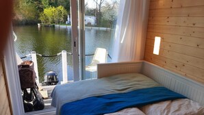 A bedroom with a bed, a view of a lake, and a boat outside. - Direkt auf dem Wasser - Un`s Lütt Goldfisch im "haifischbecken" (Röbel/Müritz)
