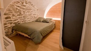 Ein Schlafzimmer mit Steinwand, Holzboden und einem Bett mit grüner Decke.