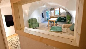 Ein gemütliches Interieur mit Essbereich, einer Couch und einer durch ein Rundbogenfenster sichtbaren Küche.