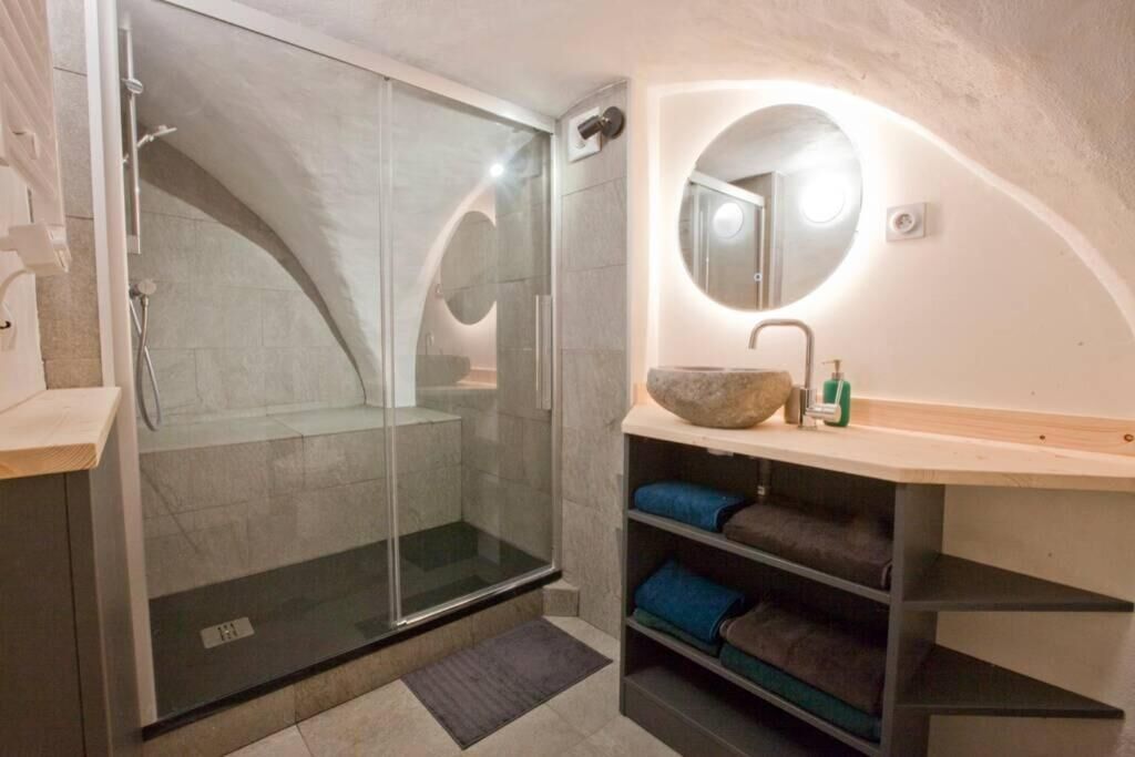Une salle de bain moderne avec une douche à parois de verre, un miroir rond et une étagère où sont pliées des serviettes.