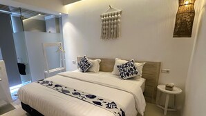 A modern bedroom with a large bed, a bedside table, a hanging light fixture, and a wall-mounted macrame piece. - Little Mykonos (Bandung)