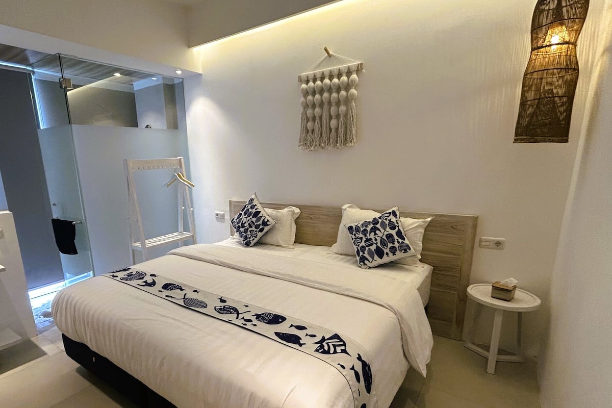 A modern bedroom with a large bed, a bedside table, a hanging light fixture, and a wall-mounted macrame piece.
