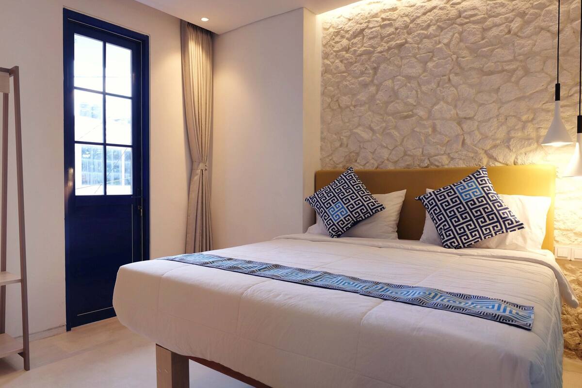 A bedroom with a bed, a wardrobe, a window, and a stone wall.