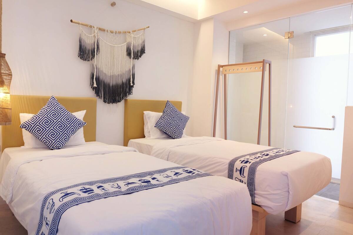 A hotel room with two beds, a large mirror, and a macrame wall hanging.