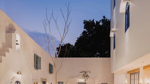 A courtyard with a central fountain, outdoor seating, and a building with multiple windows and doors. - Little Mykonos (Bandung)