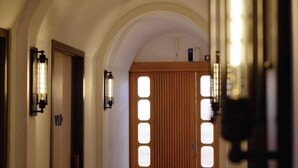 A corridor with an arched ceiling, wooden doors with rectangular windows, and wall-mounted lights. - Little Mykonos (Bandung)