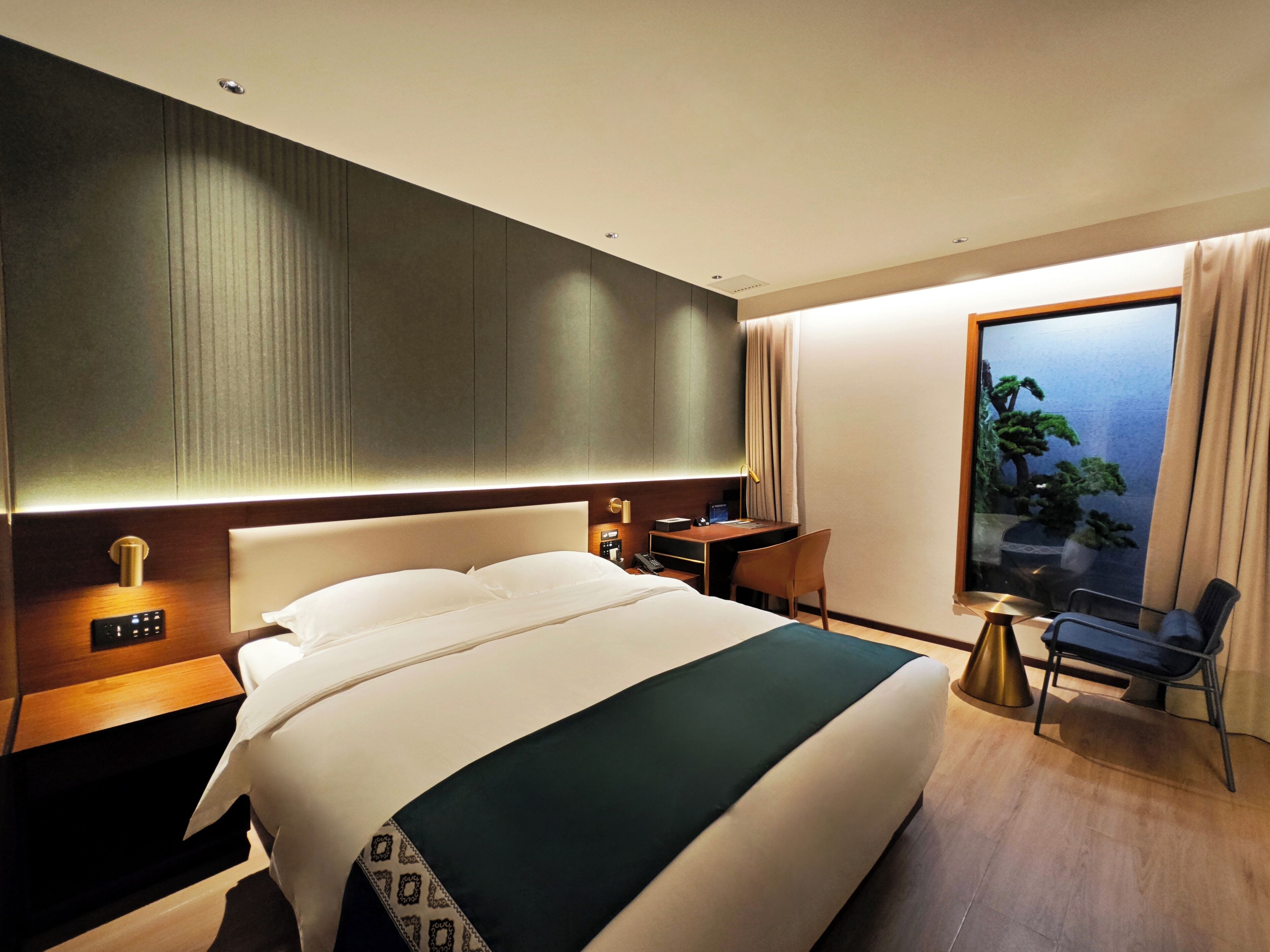 A hotel room with a large bed, a desk, a chair, a TV, and a window with a view.