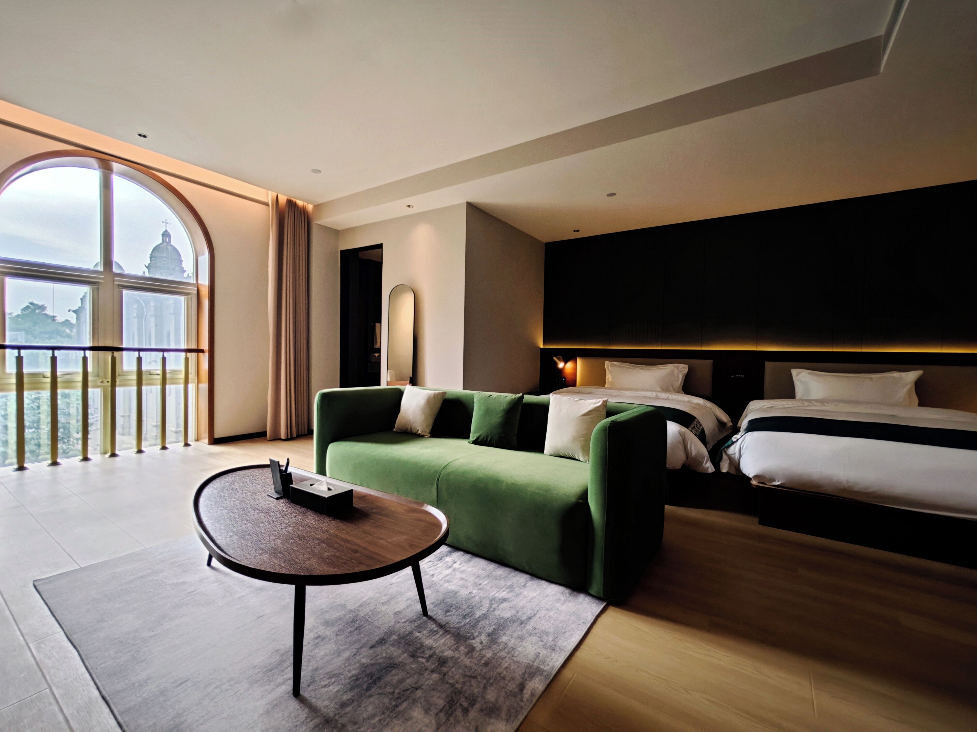 A hotel room with a large window, a green sofa, a bed, and a small table.