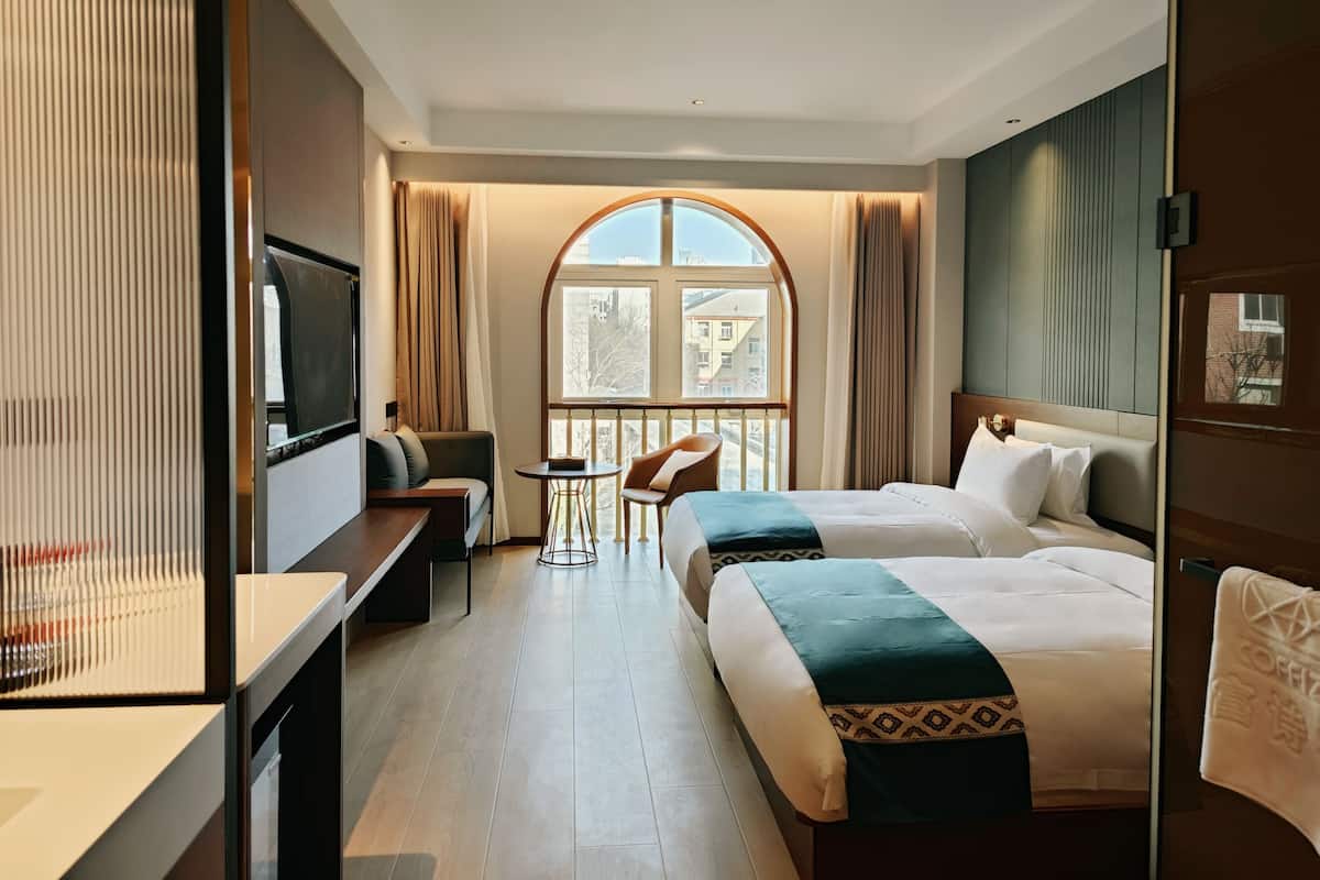 A hotel room with a large arched window, a sofa, a bed, a small table, and a TV.