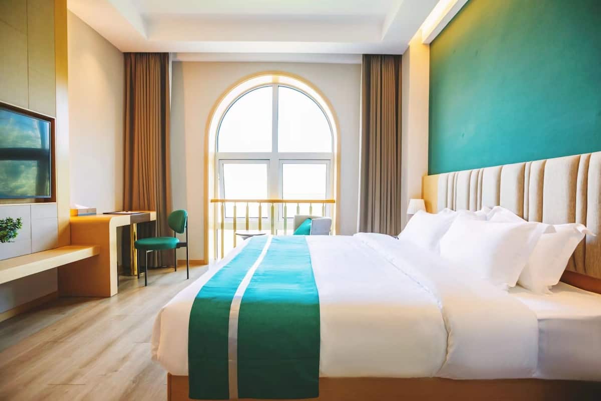 A hotel room with a large bed, a desk, a chair, and a TV.