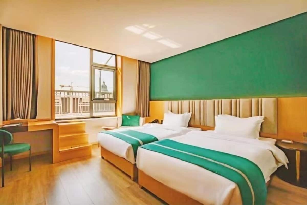 A hotel room with two beds, a desk, and a window with a view of a building.