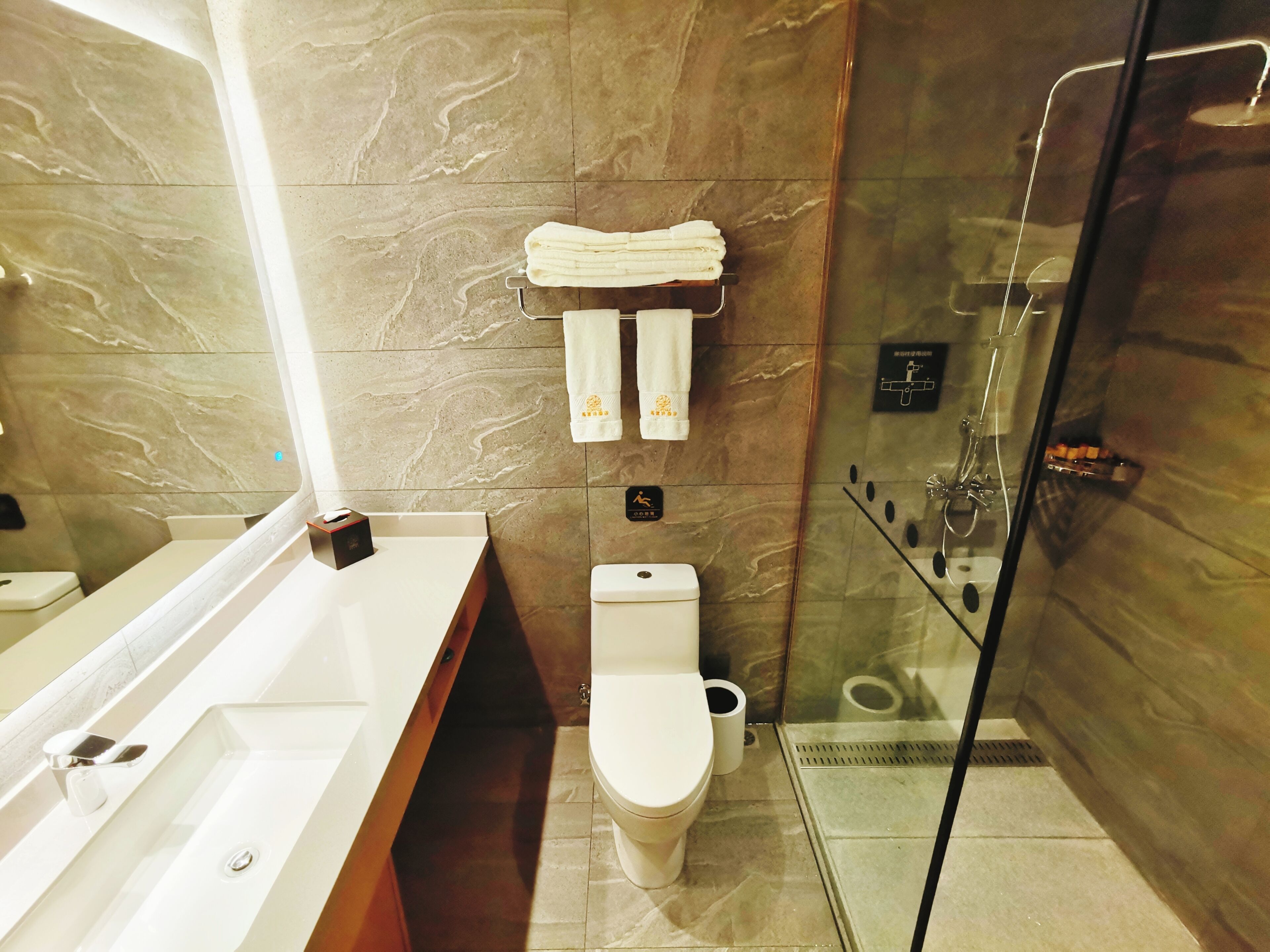 A modern bathroom with a marble wall, a glass shower enclosure, a white sink, and a toilet.