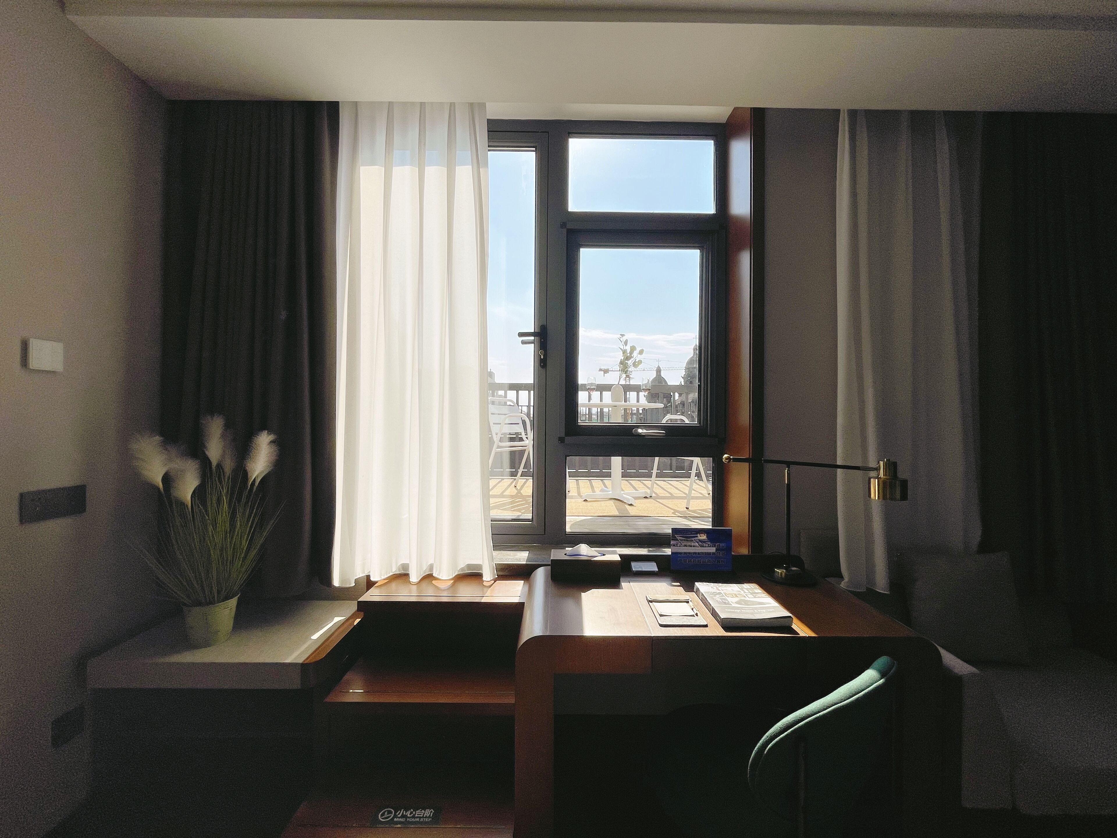 Habitación de hotel con un ventanal grande, un escritorio, una silla y una planta en maceta.