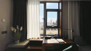 Habitación de hotel con un ventanal grande, un escritorio, una silla y una planta en maceta.