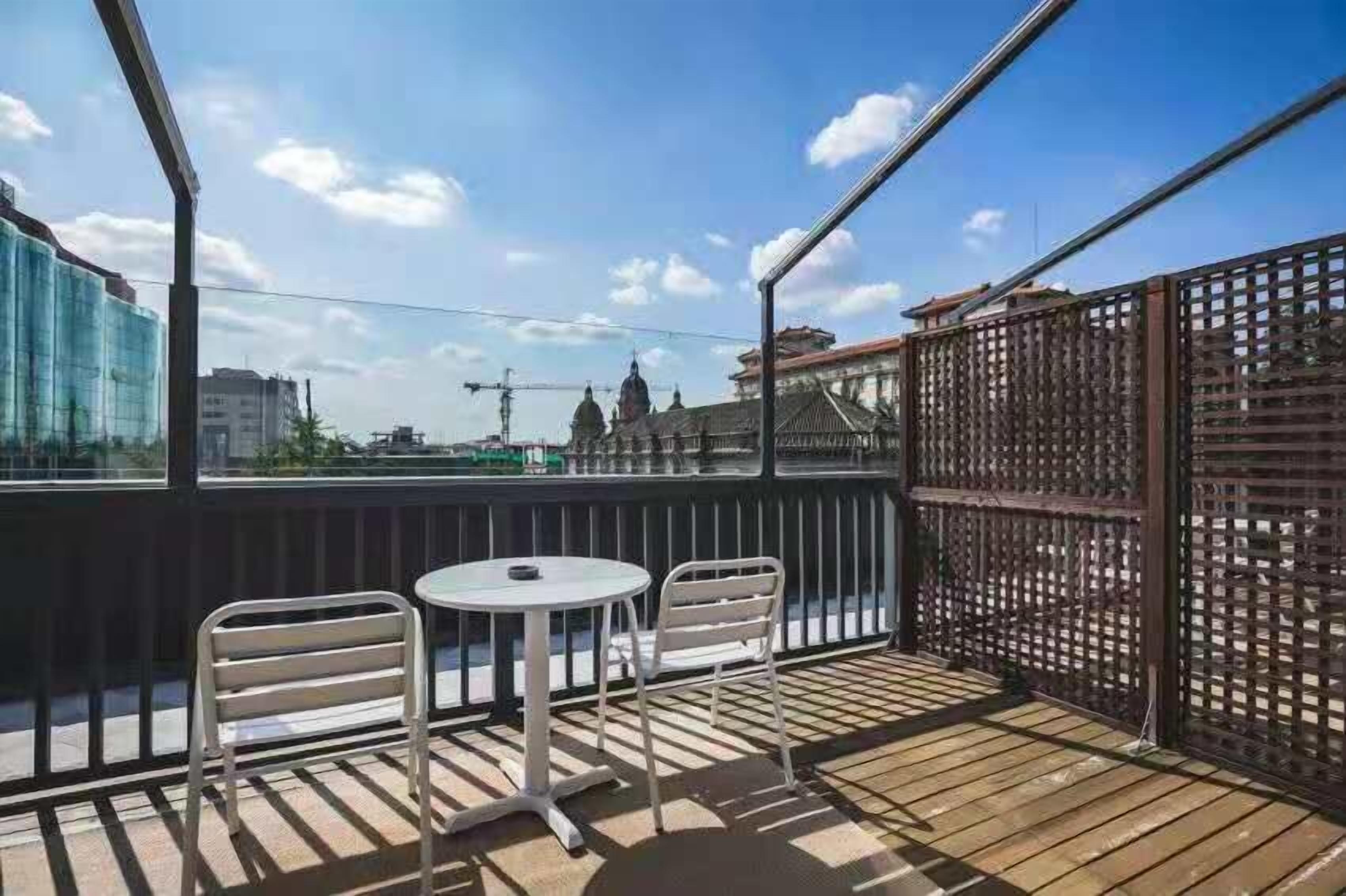 An outdoor balcony with a wooden floor, two metal chairs, and a small round table.