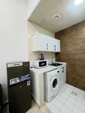 A compact kitchen with a refrigerator, microwave, sink, and washing machine. - EK Homes (Ras Al Khaimah)
