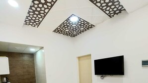 A modern living room with a sofa, a coffee table, a TV mounted on the wall, and a decorative ceiling pattern. - EK Homes (Ras Al Khaimah)