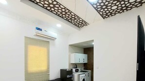 A compact living space with a sofa, a small table, a washing machine, and a kitchenette. - EK Homes (Ras Al Khaimah)