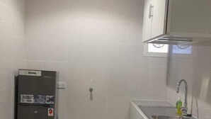 A compact kitchen with a refrigerator, sink, and white cabinets. - EK Homes (Ras Al Khaimah)