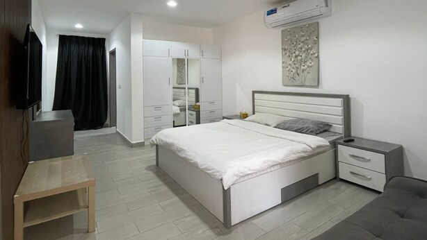 A modern bedroom with a bed, bedside tables, a TV, and a wardrobe. - EK Homes (Ras Al Khaimah)