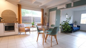 Et moderne køkken med indbygget ovn, et spiseområde med et glasbord og stole, samt en stue med sofa og planter.