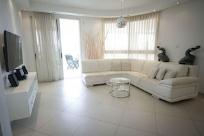 Ein modernes Wohnzimmer mit einem weißen modularen Sofa, einem Glastisch und einem Flachbildfernseher auf einer weißen Ablage.