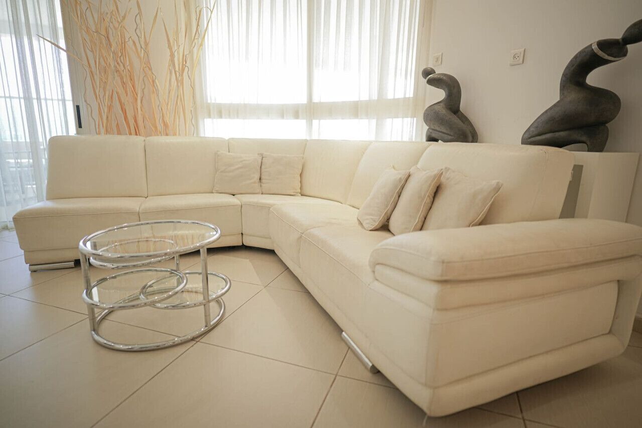 En moderne stue med en beige hjørnesofa, et glas sofabord og abstrakt vægkunst.