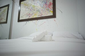 Una camera d'albergo con un letto rifatto, un quadro astratto incorniciato al muro e un asciugamano bianco sul letto.