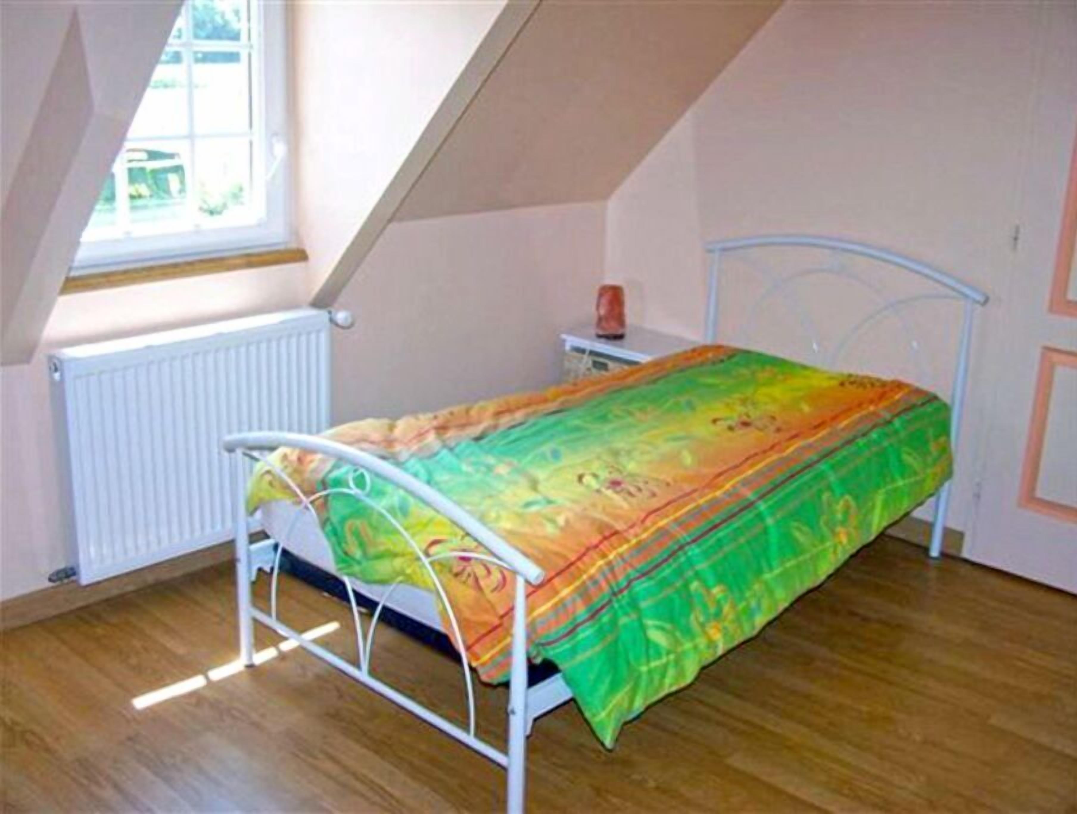 Un dormitorio con techo inclinado, una cama con colcha colorida, un radiador y una ventana con vista a zonas verdes.