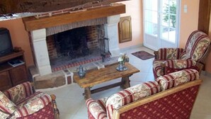 A living room with a fireplace, two patterned sofas, a wooden coffee table, and a television on a stand. - Country gite with enclosed garden located 1 hour 15 from the seaside (Mesnil-en-Ouche)