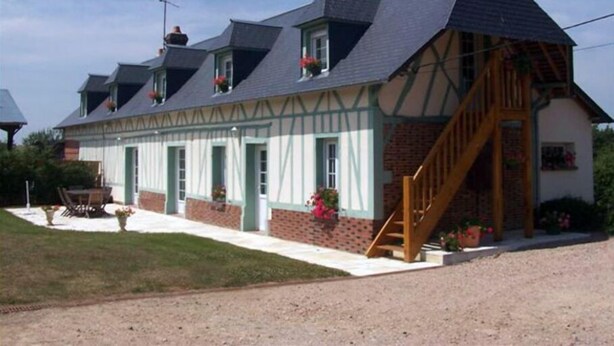 A traditional half-timbered house with a steeply pitched roof, a wooden staircase, and a front porch with a table and chairs. - Country gite with enclosed garden located 1 hour 15 from the seaside (Mesnil-en-Ouche)