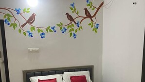 A neatly made bed with red and white bedding, a wall-mounted air conditioner, and a decorative wall decal of birds on a branch. - Ayurguru ayurvedic kalari Resort (Sulthan Bathery)