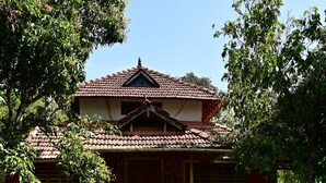 A traditional building with a tiled roof and a small porch with two white chairs. In front of the building, there is a pond with lily pads and pink water lilies. - Ayurguru ayurvedic kalari Resort (Sulthan Bathery)