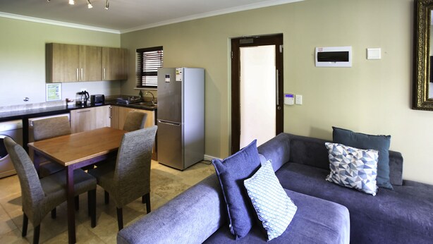 A compact living space with a dining area, a kitchen, and a seating area with a sofa and chairs. - Ellefsen Golf Suite 103 Langebaan 4-slpr (Langebaan)