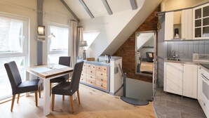A modern kitchen with white cabinets, a dining area with a wooden table and chairs, and a view of the outdoors through large windows. - FeWo Engler Doppelzimmer Gartenstraße (Lueneburg)