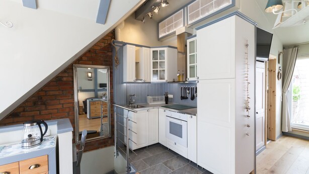 A compact kitchen with white cabinets, a built-in oven, and a hanging knife rack. - FeWo Engler Doppelzimmer Gartenstraße (Lueneburg)