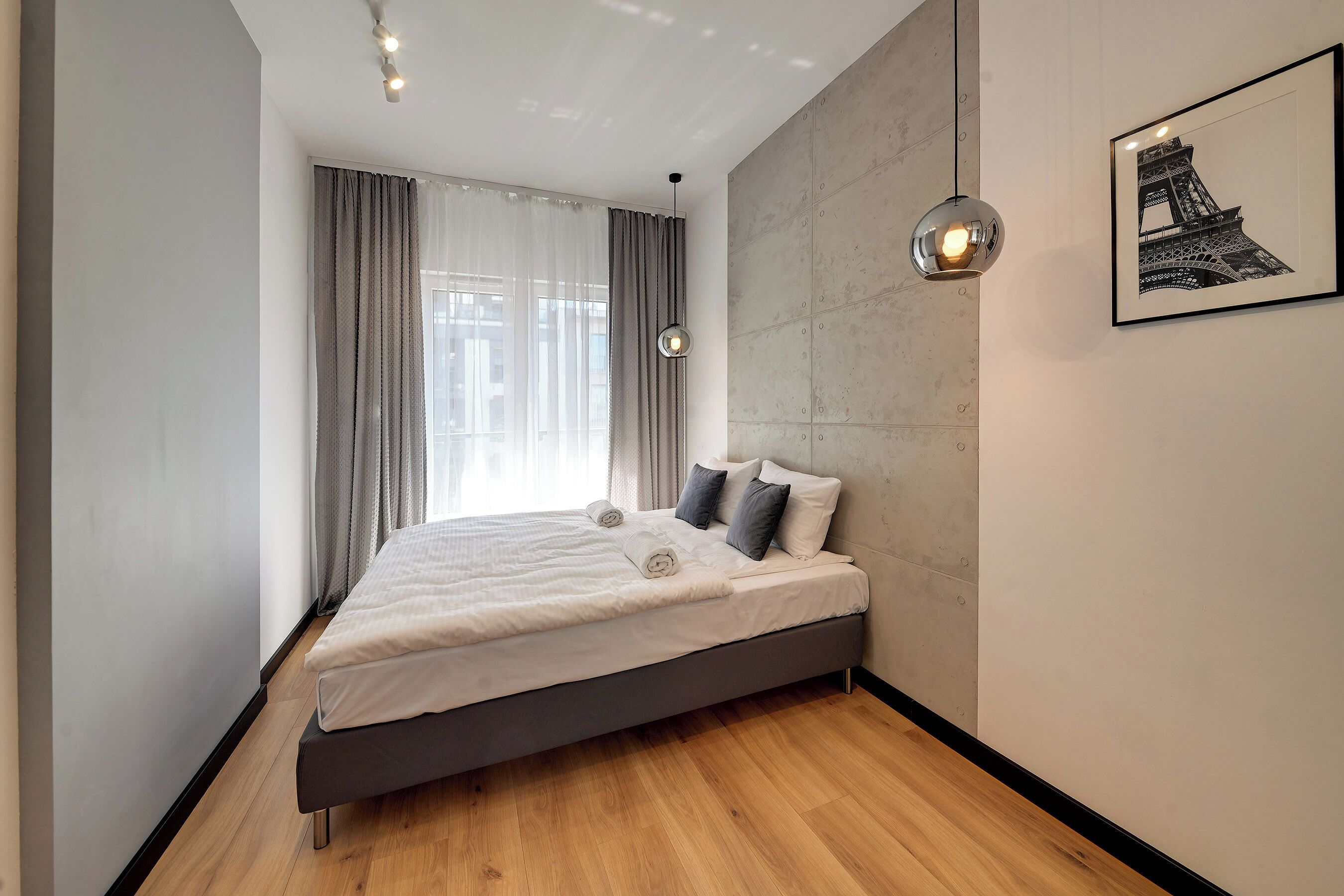 Un dormitorio moderno con una cama grande, vistas a la Torre Eiffel y una lámpara colgante.