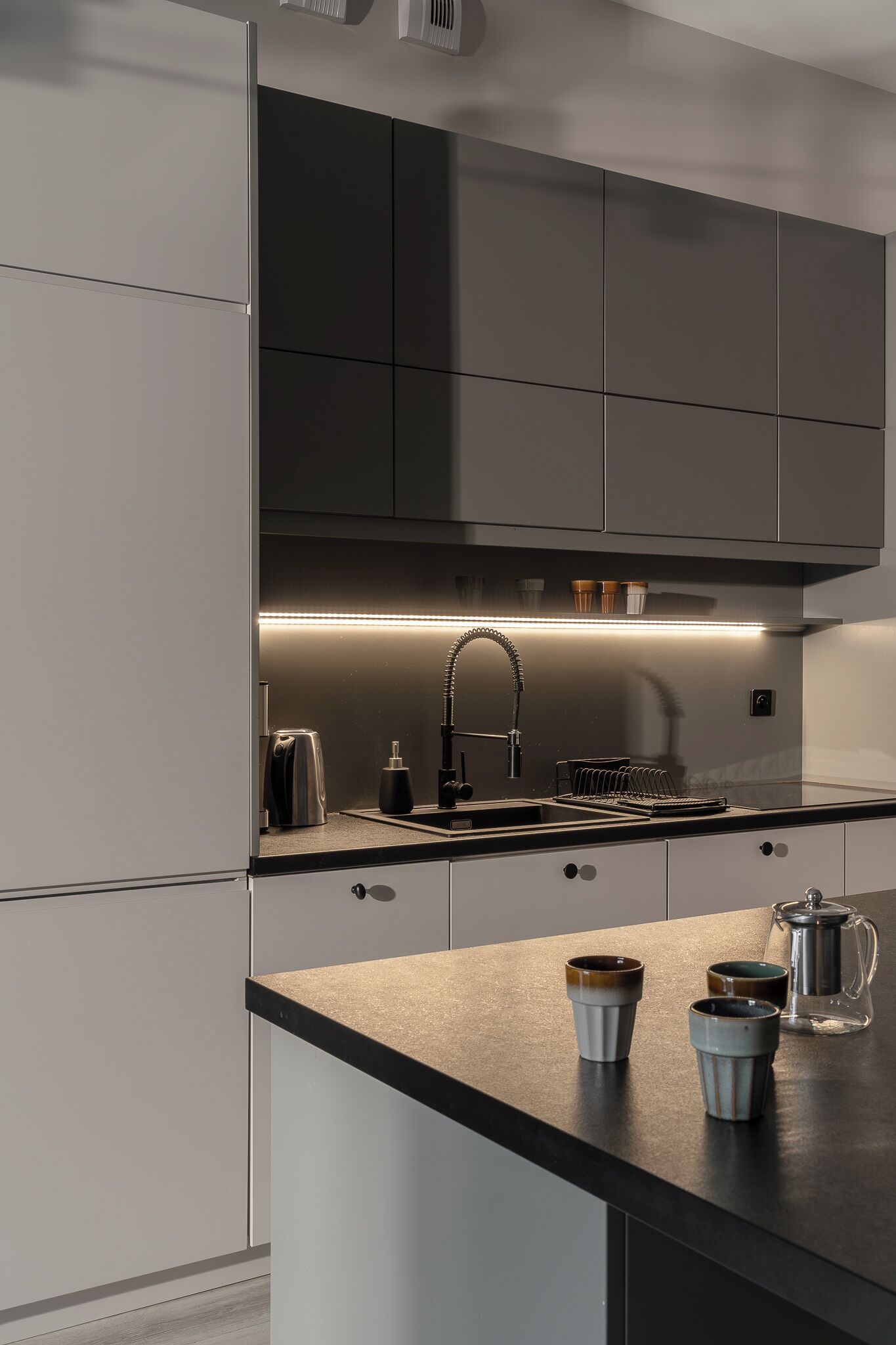 Una cocina moderna con gabinetes grises, un lavamanos de acero inoxidable y una cafetera.
