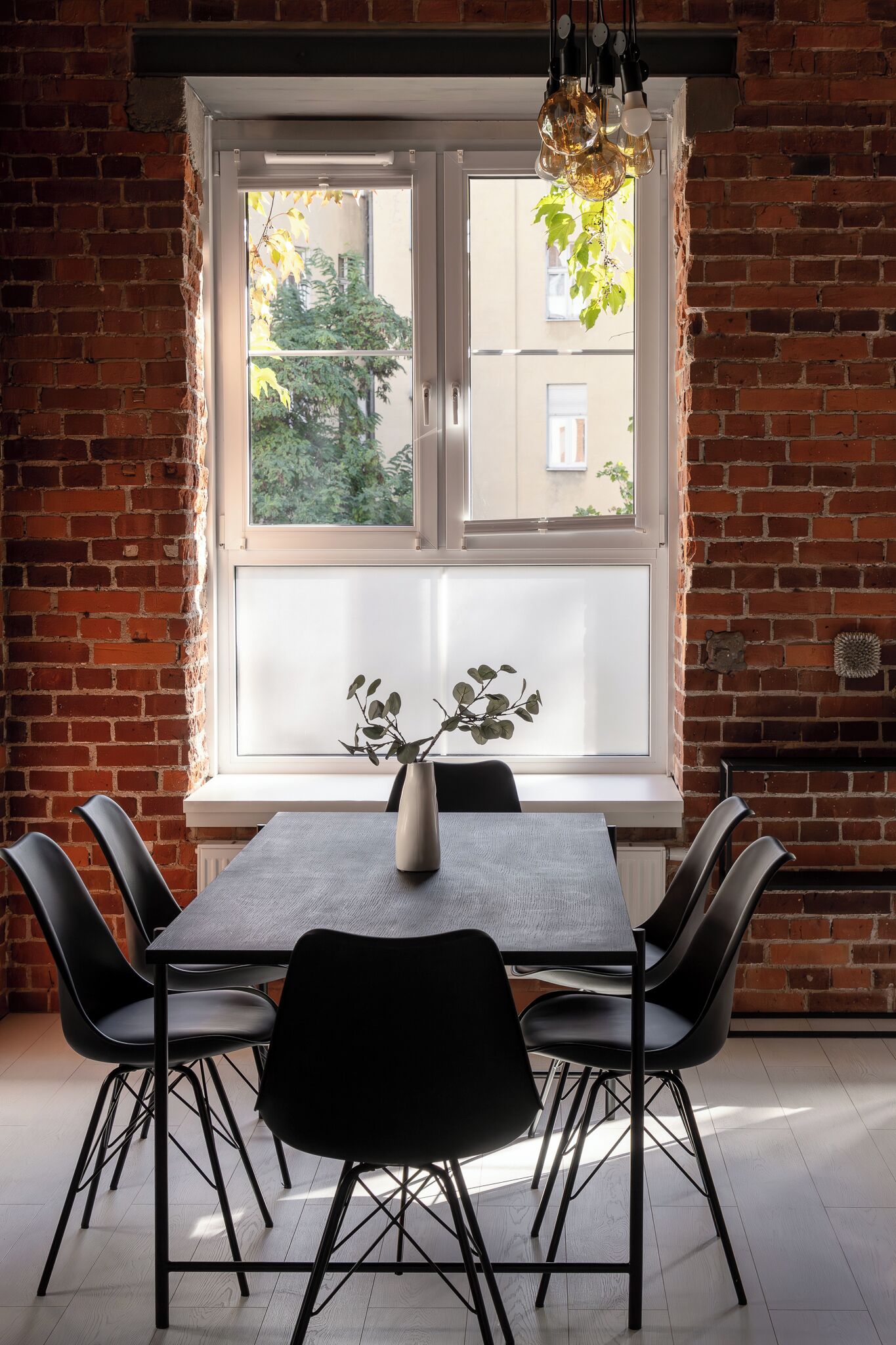 Een eetgedeelte met een bakstenen muur, een groot raam en een tafel met stoelen.